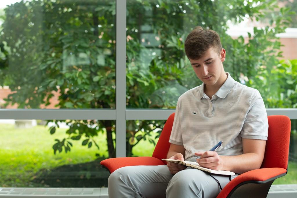 U N E student Dawson Durcotte writes a poem sitting in a chair in the Biddeford campus library