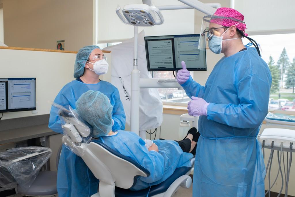 A dental student and a P A student in blue scrubs discuss dental work with a patient