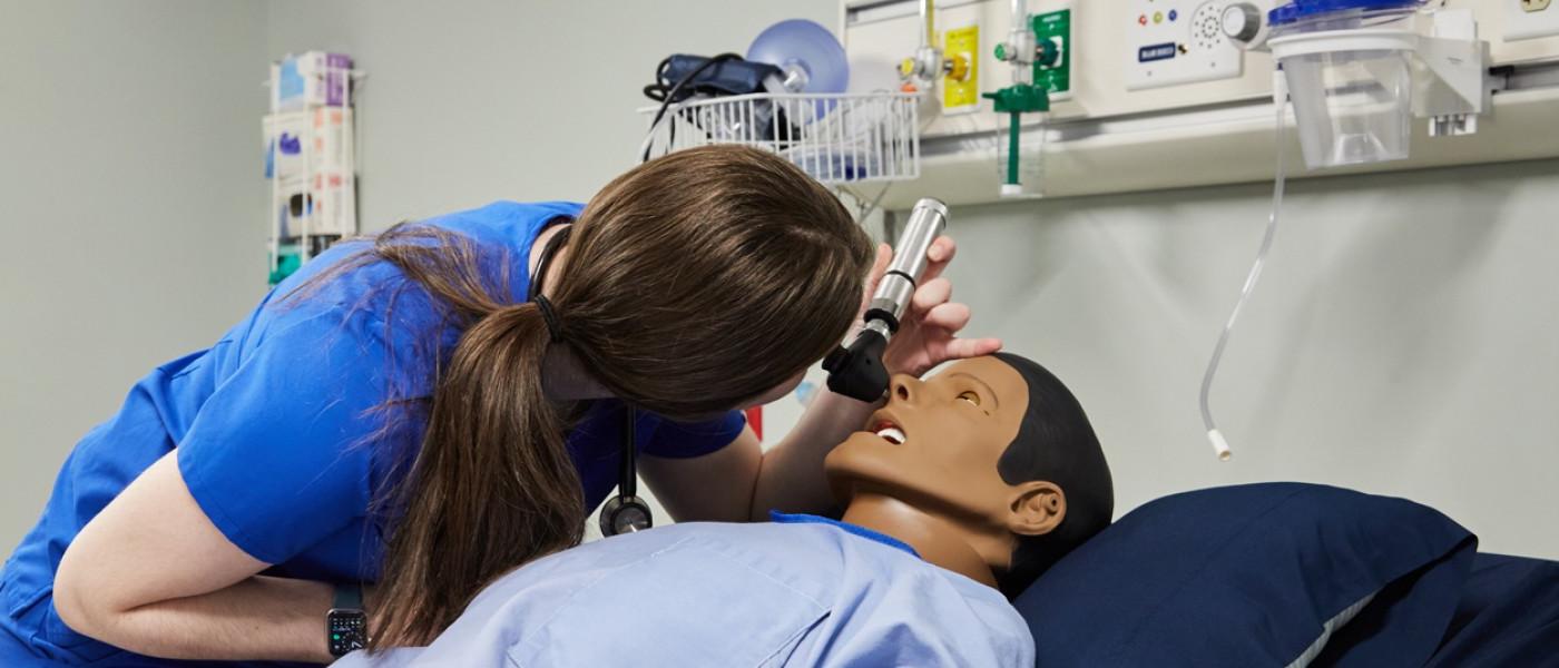 A physician assistant student uses an otoscope on a patient simulator