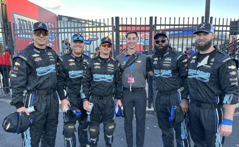A UNE student poses with a group of race car drivers